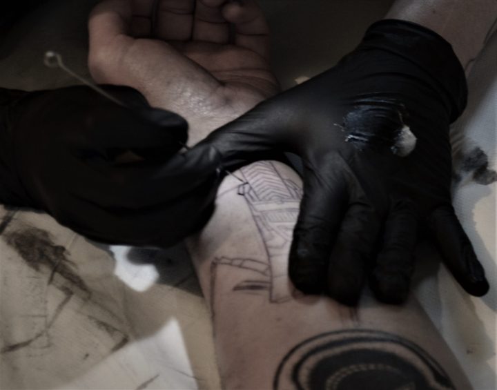 Photo d'une tatoueuse en train de tatouer à la main un motif de claptrap du jeux video borderland. Tatouage handpoke