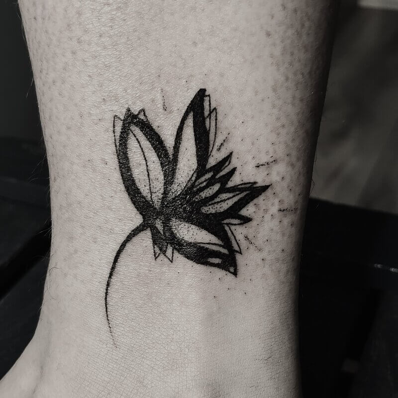 Un tatouage graphique noir en handpoke avec des lignes abstraites d'une fleur sur la cheville