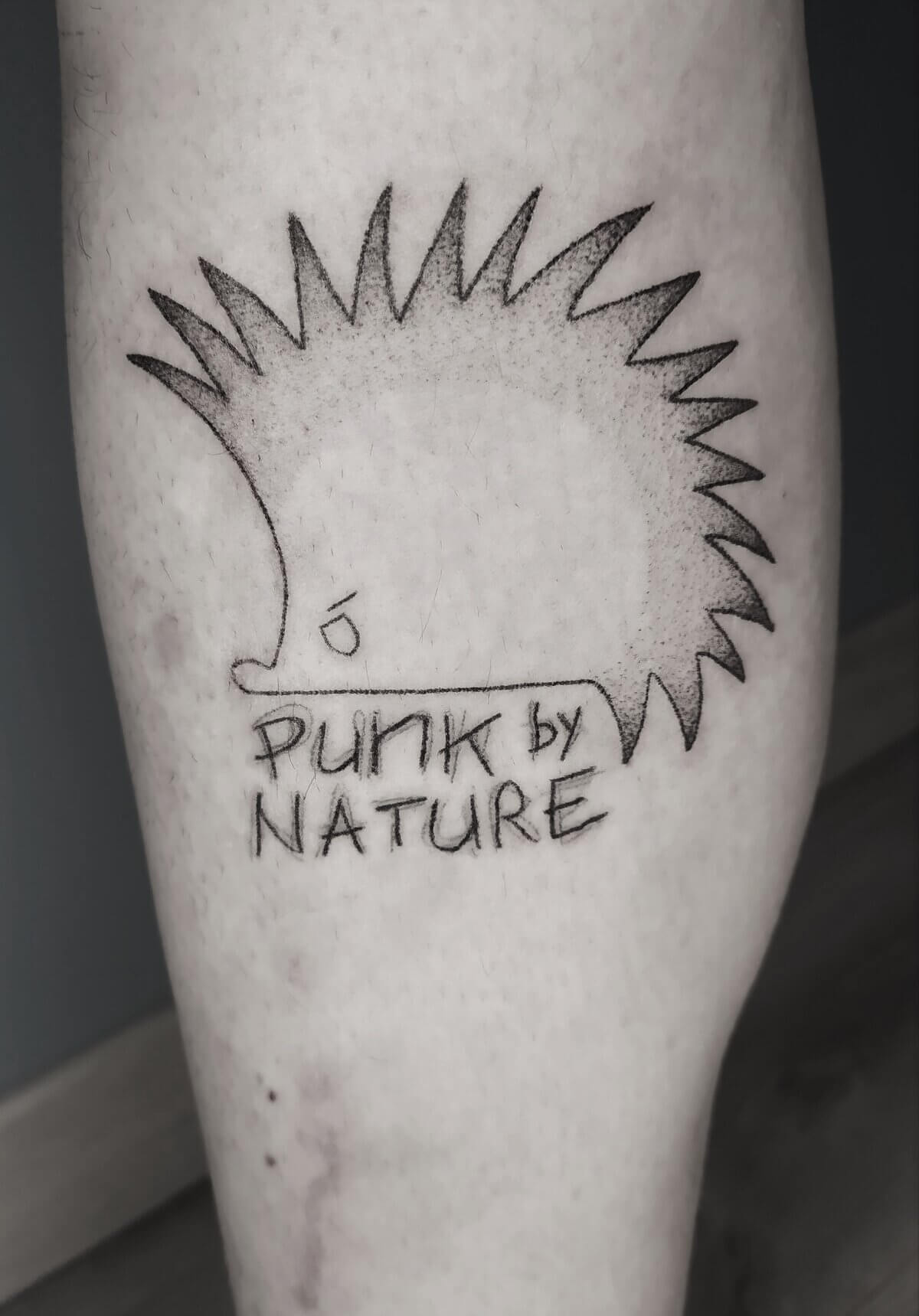 Un tatouage handpoke d'un dessin de hérisson avec marqué Punk by nature sur le mollet