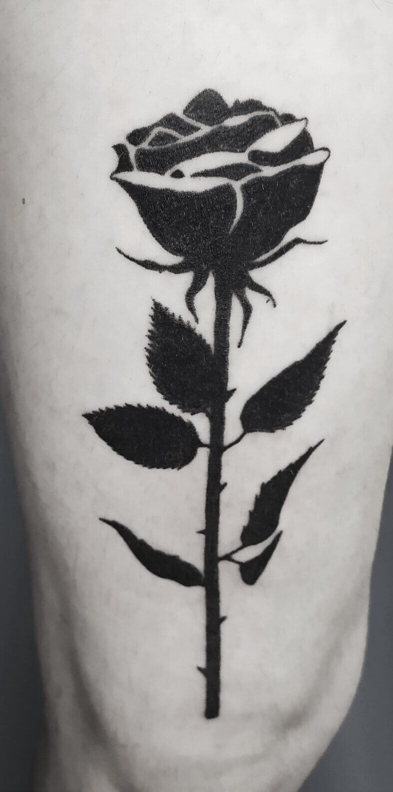 Un tatouage handpoke noir d'une fleur de type rose sur la cuisse