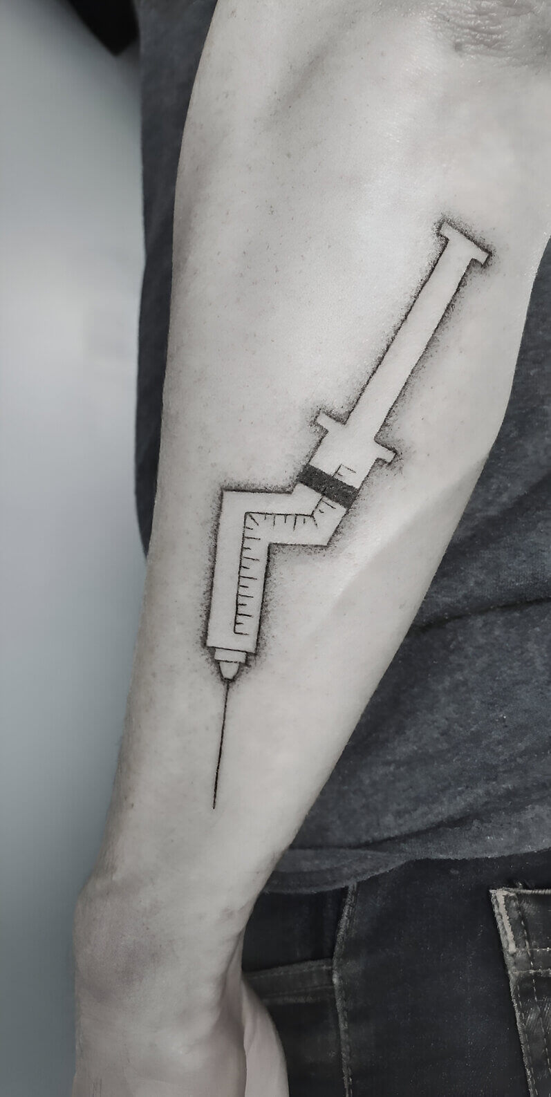 Un tatouage handpoke d'une seringue brisée sur l'avant bras